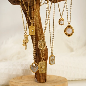 Détail de colliers en titane doré avec pendentifs rose, cœur et perle sur un support en bois