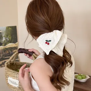 Detail van crème kanten scrunchie met rode kersenborduring en gehaakte textuur