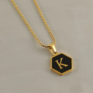 Detail of a gold hexagon pendant with the letter K on a delicate stainless steel chain