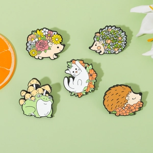 Flat lay of colorful hedgehog, frog, and cat enamel pins on light green background