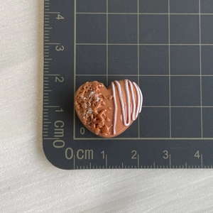Macro detail of a 1.5cm heart-shaped resin bread charm with nut texture and white drizzle