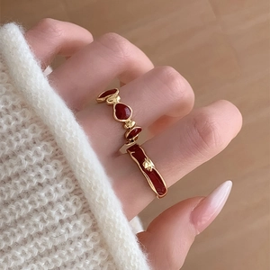 Close-up of stacked gold rings with red enamel hearts on a hand with white sweater