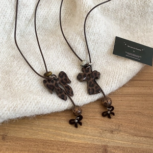 Détails des pendentifs nœud et croix léopard sur un collier vintage en cordon marron