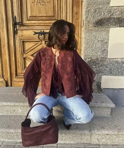 Detail of embroidered burgundy velvet vest with bohemian ruffles and vintage leather bag