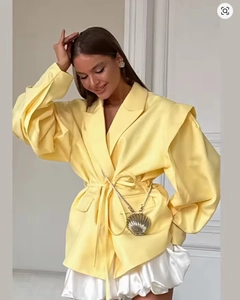 Détail d'un blazer oversize jaune clair avec ceinture et sac à main en métal en coquillage