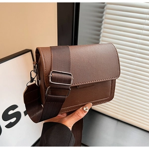 Detail of dark brown rectangular flap bag with a wide adjustable nylon shoulder strap