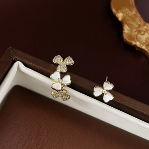 Macro view of gold plated asymmetric flower earrings with white enamel and zircons