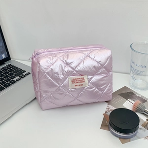 Lifestyle shot of a pale pink quilted makeup bag on a white desk with daily accessories