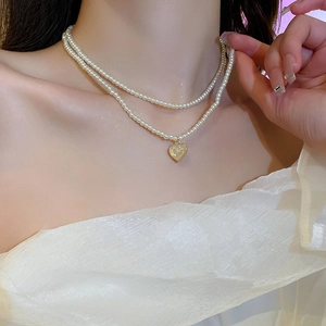 Detail shot of a double-layered pearl necklace with a gold heart pendant on a model