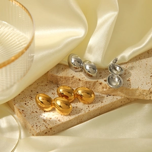 Boucles d'oreilles goutte polies or et argent sur satin beige et pierre de travertin
