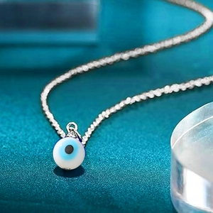 Close-up of a blue Evil Eye charm pendant on a silver-toned stainless steel chain necklace