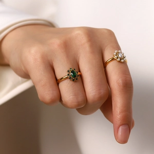 Elegant gold ring set featuring emerald gemstone and pearls shown on a woman's hand