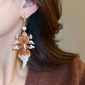 Detail of goldfish enamel earrings with pearls worn by a model in warm light