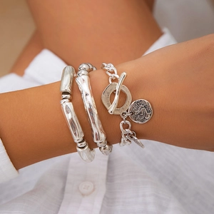 Close-up of three silver-tone bracelets including a coin pendant and hammered bangles