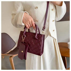 Detail of burgundy quilted handbag with matching coin purse and golden hardware on a model