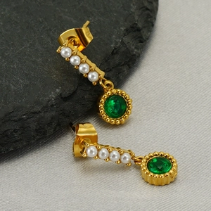 French style gold pearl earrings with a green zircon drop on a textured stone background