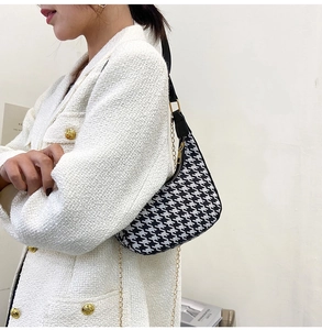 Detail of houndstooth baguette bag with black leather strap and gold chain detail