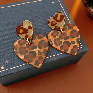 Macro shot of stylish leopard print double heart acrylic earrings on blue jewelry box