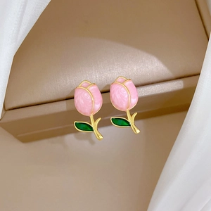 Macro detail of tulip earrings with pink enamel flower buds and golden stems in a box