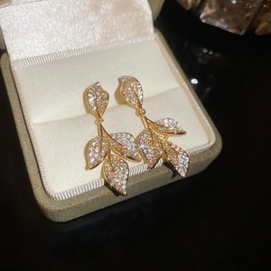 Macro detail of golden leaf-shaped tassel earrings with pavé zircons in a jewelry box