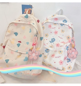 Detail of canvas backpacks featuring colorful prints and pink floral plush charm accessory