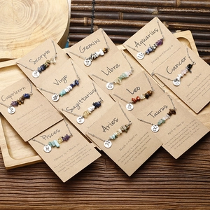 Close-up of 12 Zodiac necklaces with natural raw stones and engraved metal tags on paper