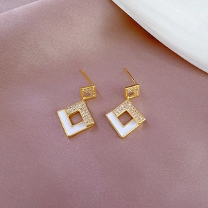 Close-up of golden geometric earrings with white enamel and micro-set zircon accents