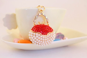 Detailed close-up of a golden handbag keychain featuring red rhinestones and white pearls