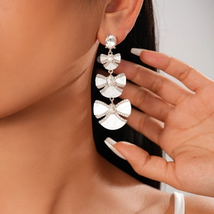 Detail of elegant silver drop earrings with white resin bow shapes on model