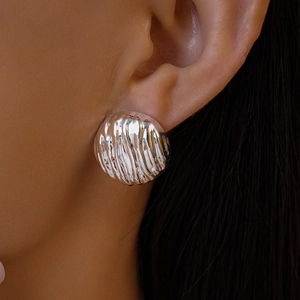 Gros plan d'une boucle d'oreille ronde argentée à texture ondulée sur l'oreille