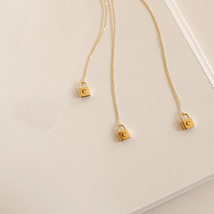 Detailed macro view of gold padlock pendant with letter C on a stainless steel chain