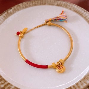 Détail du bracelet gourde dorée avec fil rouge, pompon et breloque cadenas de chance
