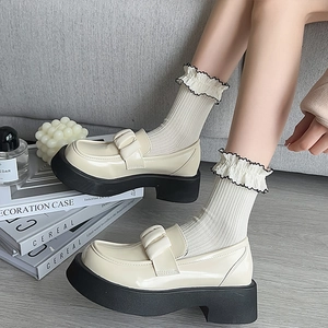 Chunky cream patent loafers with black platforms styled in a minimalist aesthetic scene