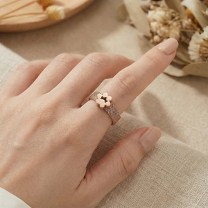 Detail of rose gold mesh ring with flower charm worn on finger over soft fabric