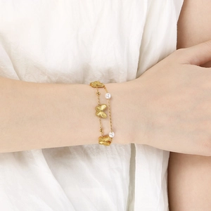 Detail of a double-layered gold butterfly and pearl bracelet worn on a woman's wrist