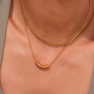 Close-up of layered 18K gold plated necklace with snake chain and small ring pendants