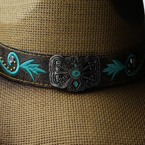 Detail of straw cowboy hat featuring a silver butterfly buckle and turquoise embroidery