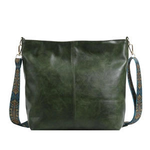Dark green leather bucket bag with an embroidered ethnic wide shoulder strap on white backdrop