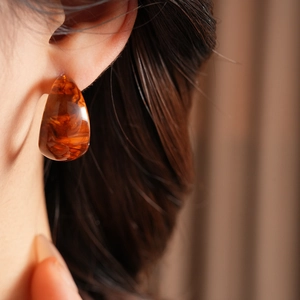 Close-up of model wearing C-shaped amber resin earrings with a retro marbled texture