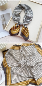 Détail d'un foulard en soie rayé jaune moutarde noué en nœud et posé à plat avec soin