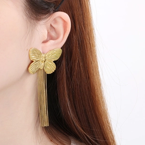 Close-up of golden butterfly earrings with long tassel chains worn by a female model
