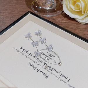 Detail view of silver bow earrings with tassel and inlaid zircon on a white plate