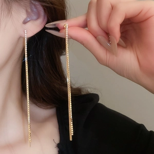 Detailed close-up of golden tassel earrings with white rhinestones on a female model