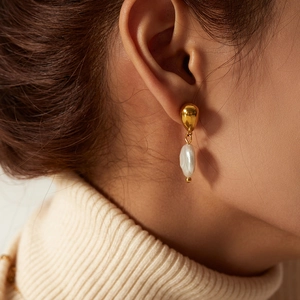 Elegant gold drop earrings with white baroque pearl pendants shown on a model