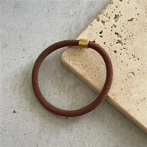 Detail of a brown woven elastic hair tie with a gold metal fastener on a stone base