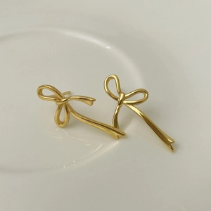 Detailed view of elegant gold bow earrings placed on a minimalist white ceramic tray