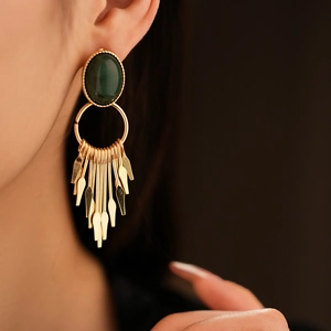 Detail of vintage gold tassel earring with green gemstone on a model with soft lighting