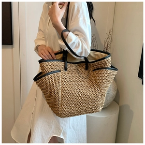 Close-up of a large straw tote bag featuring contrast black leather trim and side pockets