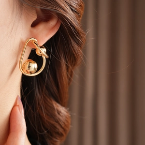 Close-up of stylish twisted gold ball earring on a model for an elegant metal look