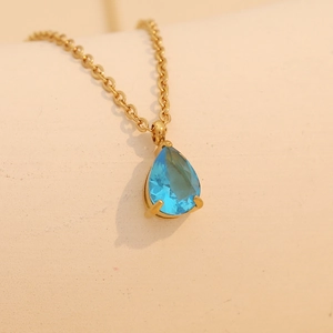 Golden necklace featuring a light blue pear-cut gemstone pendant with a faceted finish
